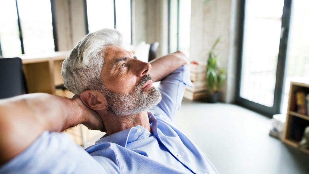 A thoughtful mature businessman with gray hair in the office wearing a blue shirt.