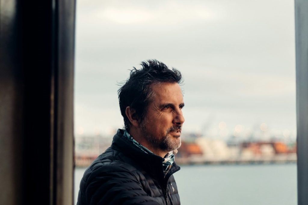 A man in a black jacket is standing near a body of water during the daytime.