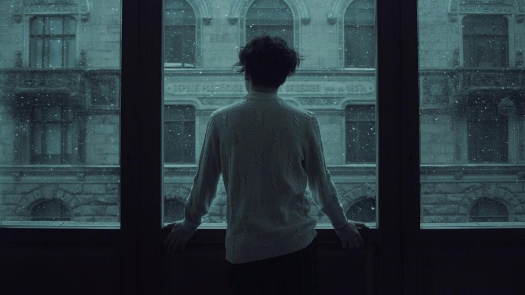 A man staring out of a window that is speckled with raindrops.
