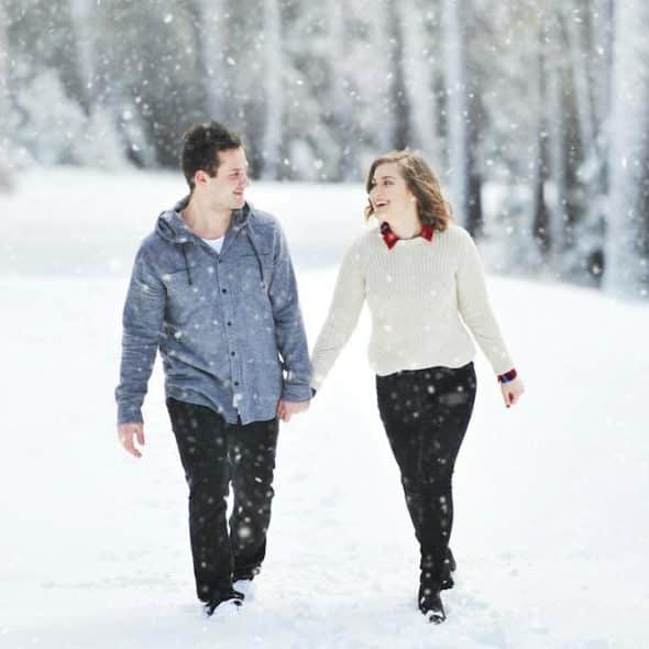 A couple walking on snow near trees during daytime.