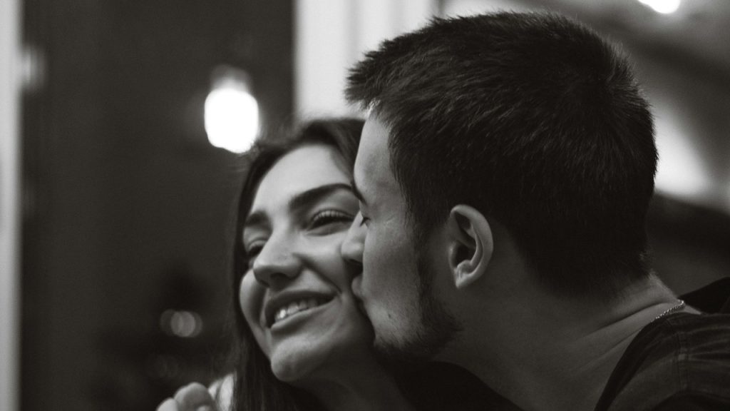 A man kissing a smiling woman.