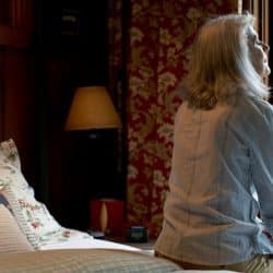 A woman sitting on the bed in front of a window in the morning.