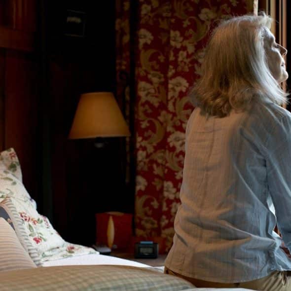 A woman sitting on the bed in front of a window in the morning.