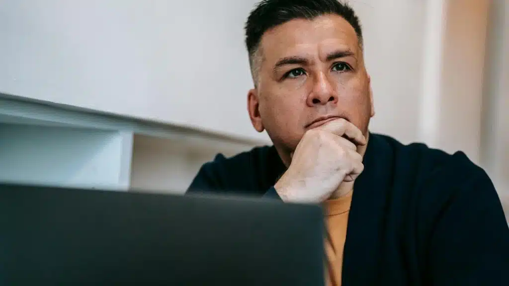 A man resting his chin on his hand, looking thoughtful while sitting at a desk.