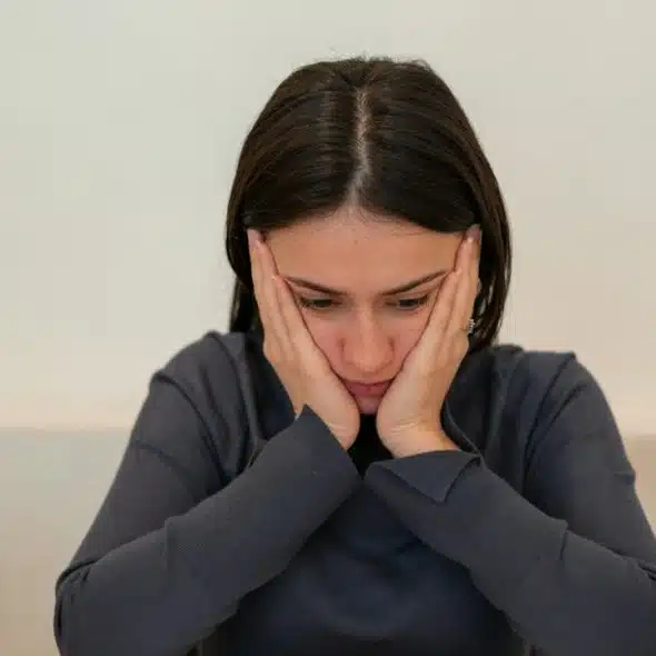 A worried woman is sitting at a table with her face in her hands.