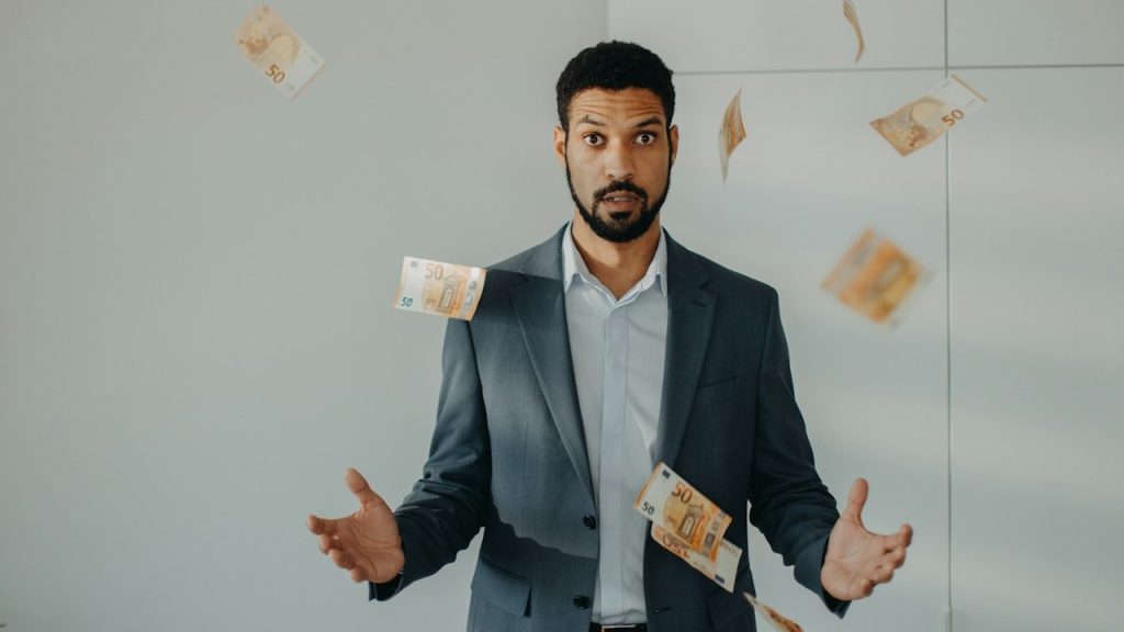 A serious young businessman standing in office throwing money away.