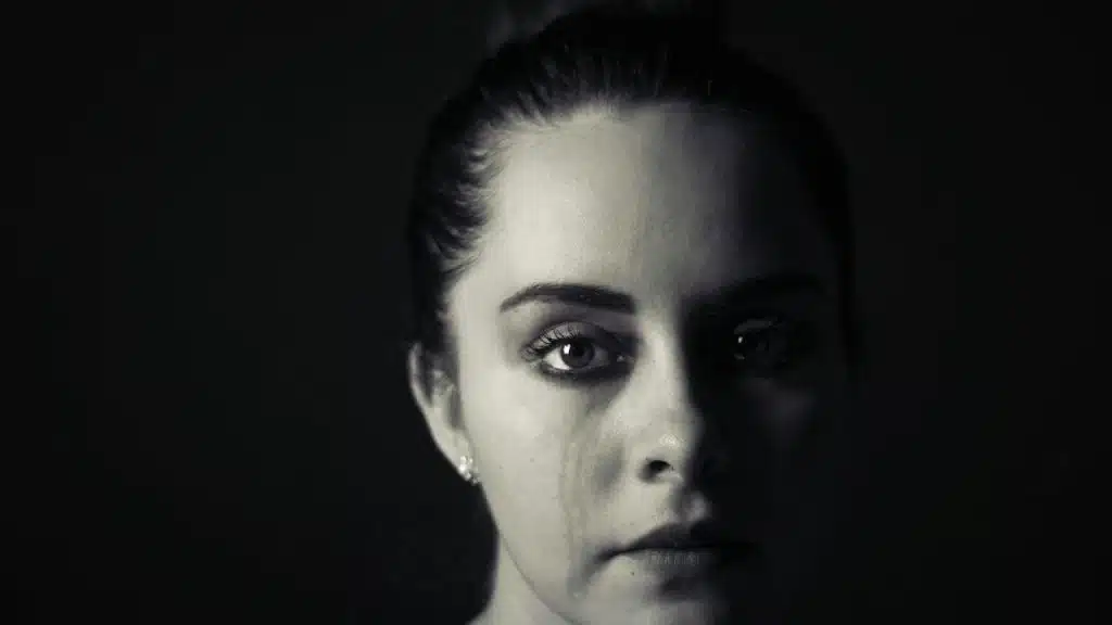 A woman is staring at the camera with tear stains on her cheek.