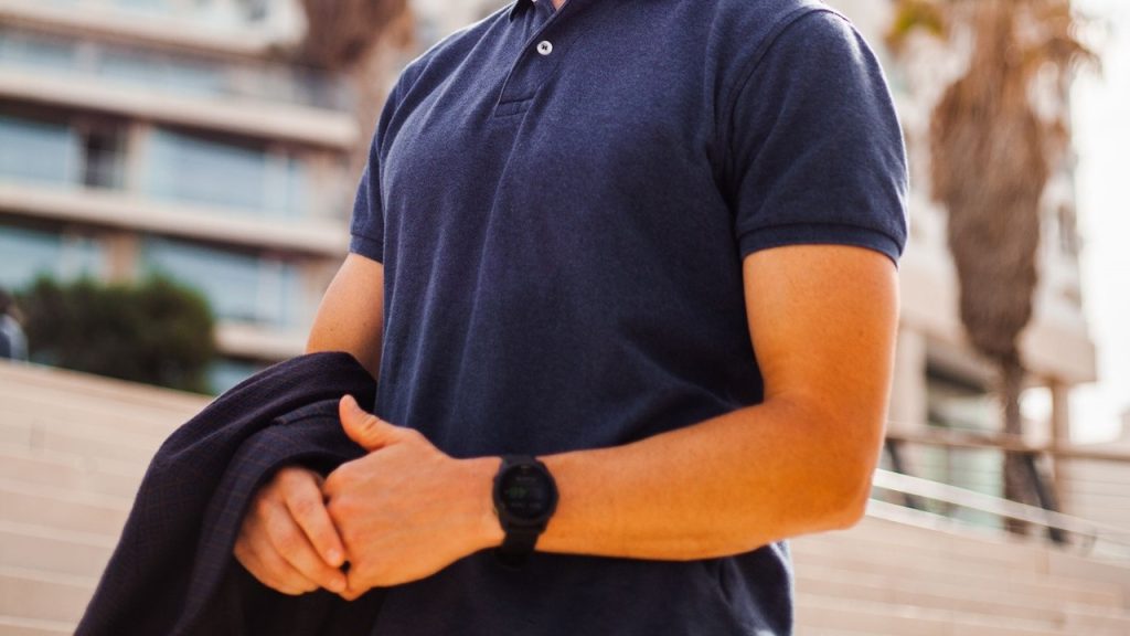 Smiling man with black polo shirt and a stylish watch is walking down a street.