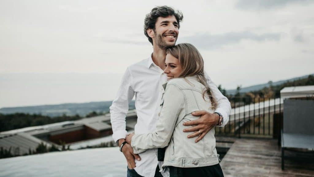 A smiling couple hugging each other while standing on the top of a building.