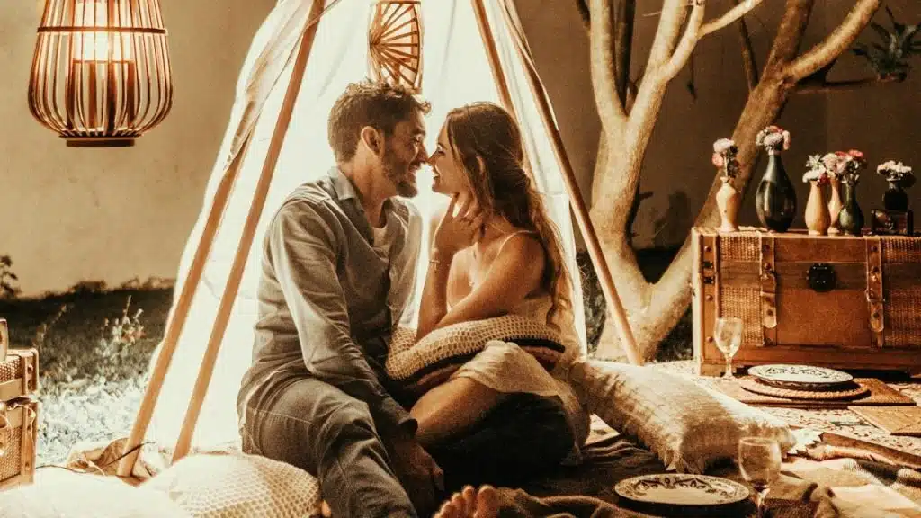 A couple sitting in a makeshift tent in their living room and sharing a tender moment.