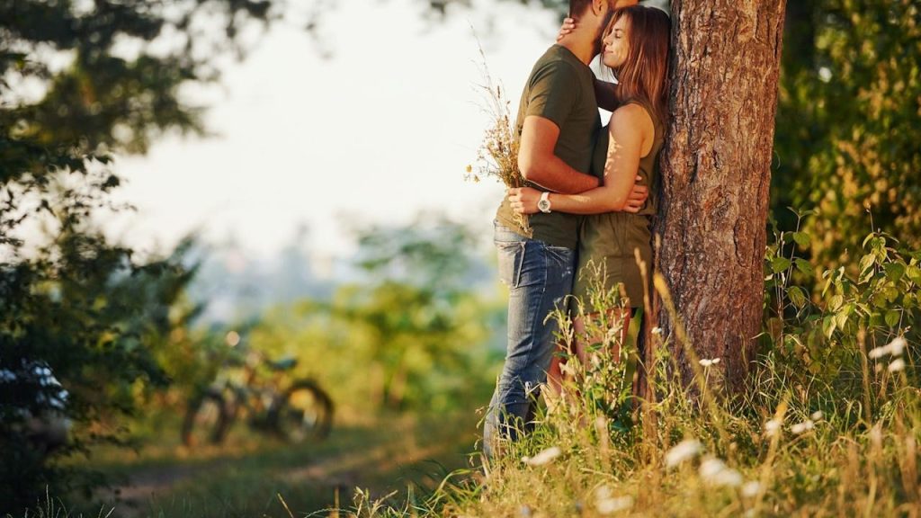 A couple hugging while they are leaning on a tree.
