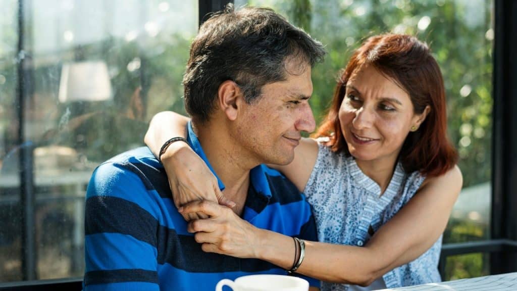 A woman putting her arms on the shoulders of a man while they are having coffee outdoors.