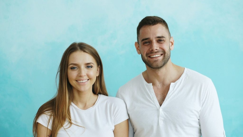 A smiling couple in white shirts against a blue background.