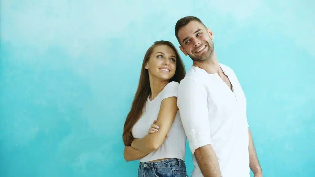 A couple standing back-to-back against a blue wall.