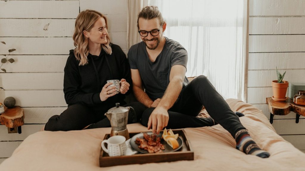 A couple having breakfast together while sitting on bed.