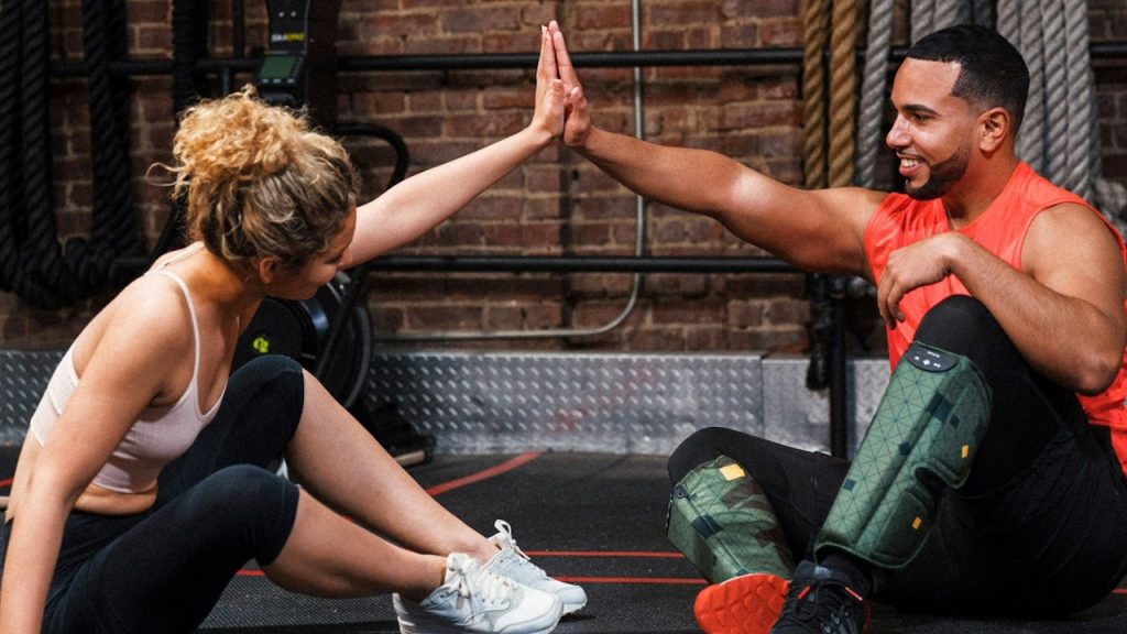 A couple is high-fiving each other as they sit on the floor of a gym.