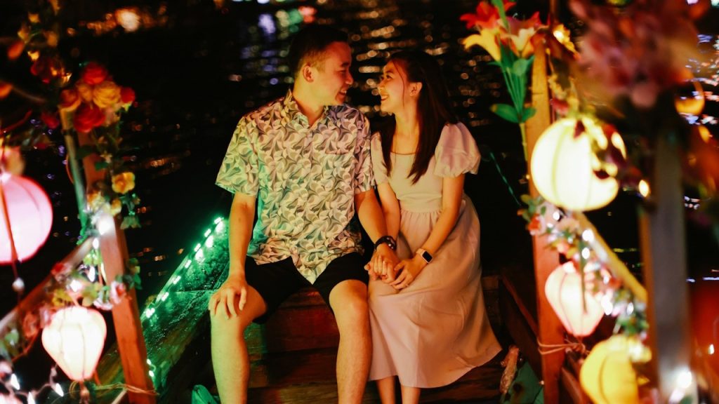 A couple sitting in a decorated boat and smiling at each other.