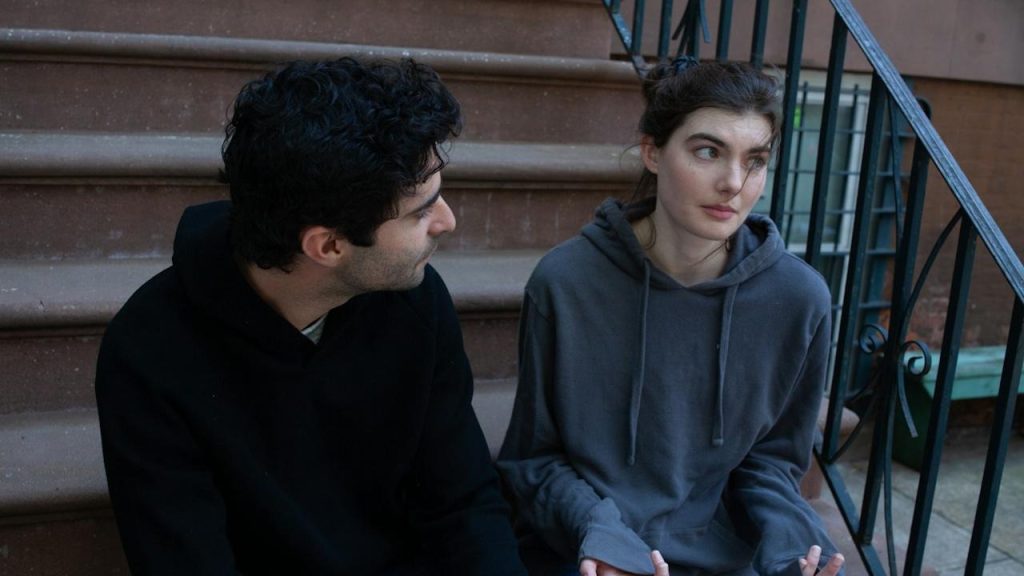 Man and woman sitting on a stoop or steps, looking serious while having a conversation.
