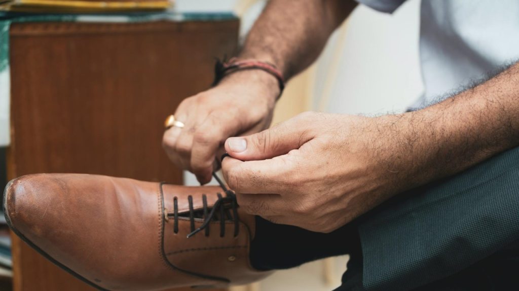 A person tying his brown-colored shoe.