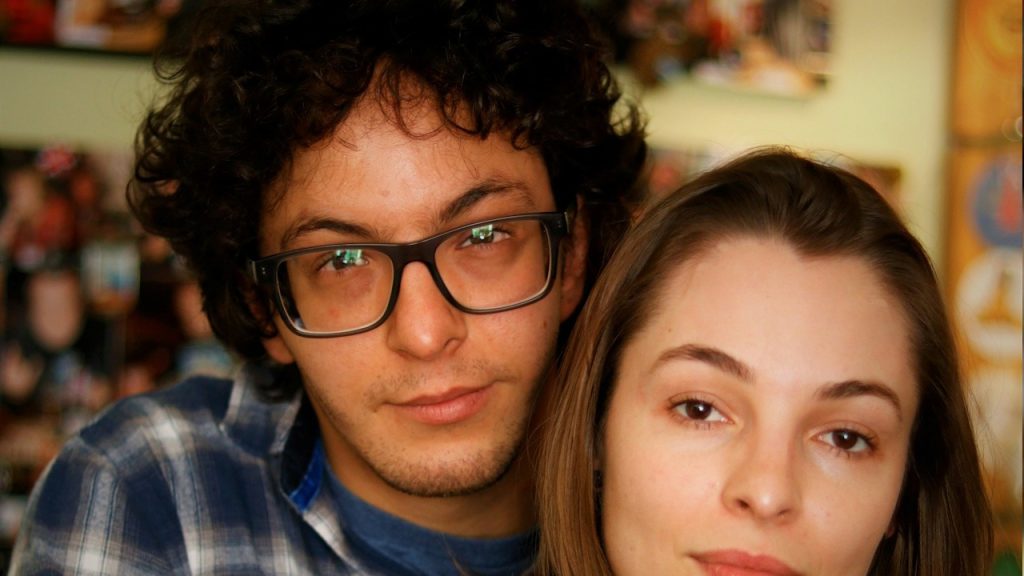 A man-in-blue-and-white-plaid dress shirt beside a woman in a black shirt.