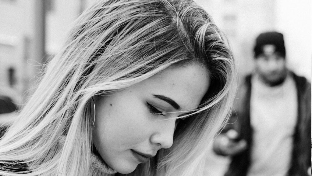 A stylish woman is looking downwards, and a man is coming towards her.