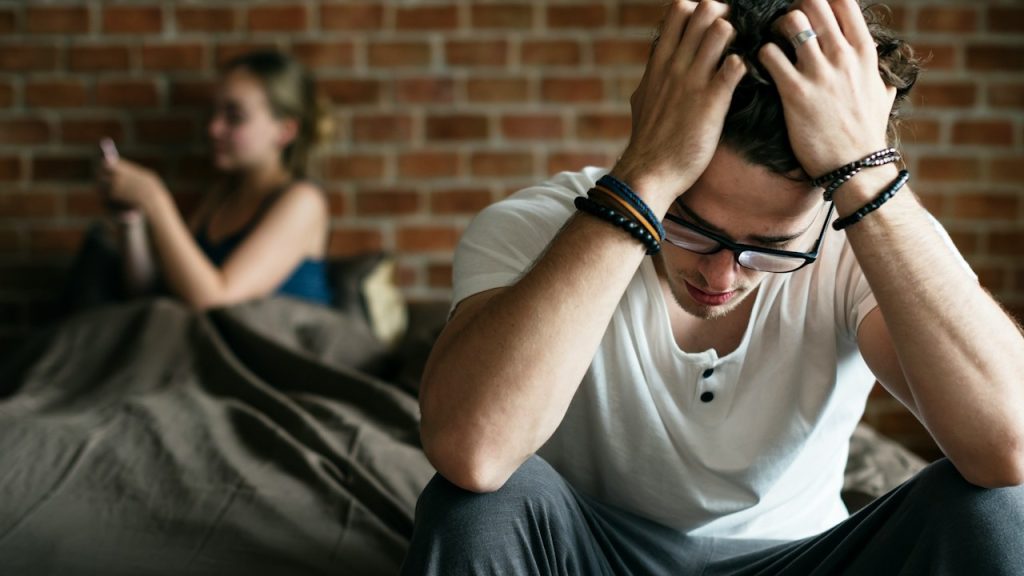 The frustrated man while a women using a phone behind him