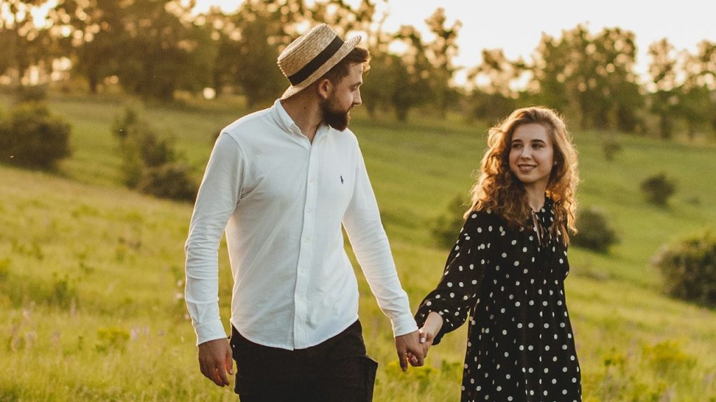 A man in a white dress shirt and a woman in a black dress are standing on a green grass field.