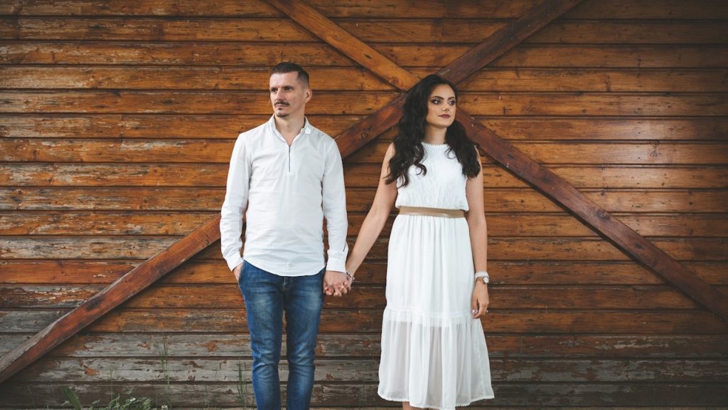 A couple holding hands in front of a wooden wall.