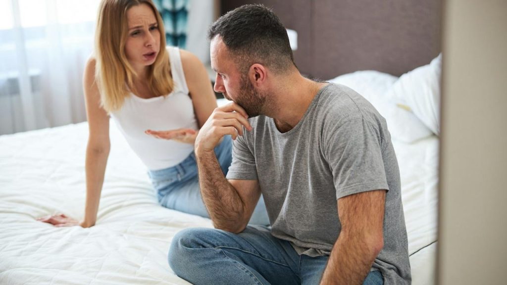 A displeased lady is talking to her husband while her husband touches his chin.