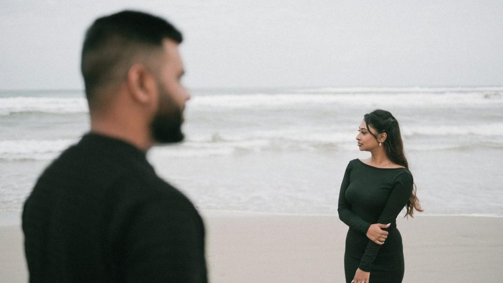 A couple on the beach are facing the ocean.