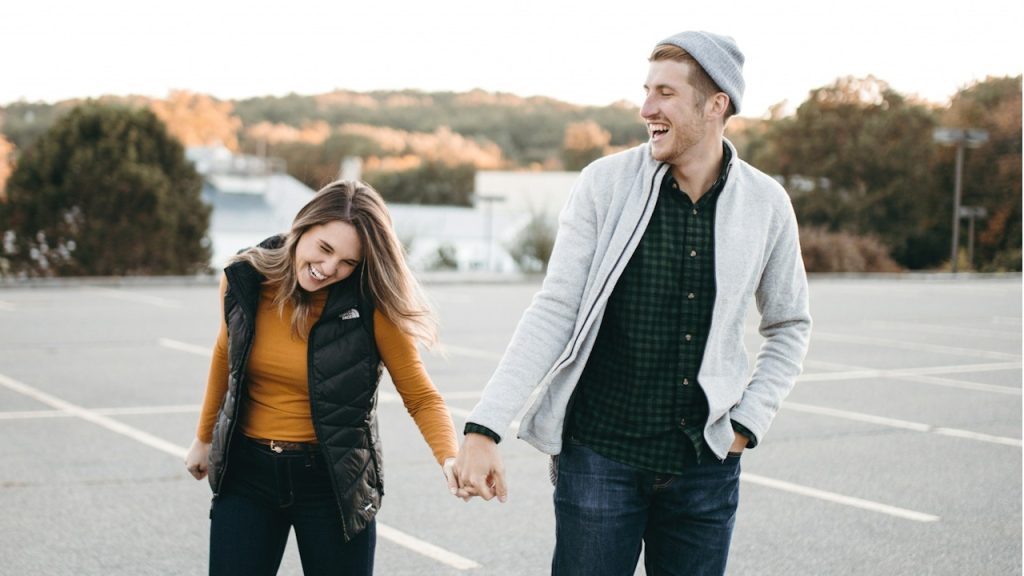 A man and a woman holding hands and laughing while walking.