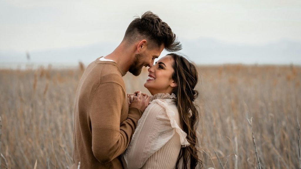 A couple looks at each other lovingly in a field.