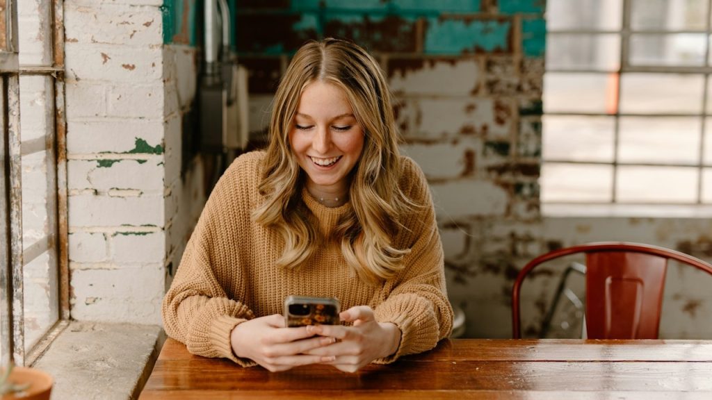 A blond woman smiling and looking at her phone.