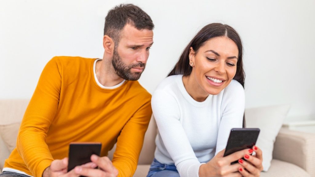A man is spying on his wife who is texting on her cellphone.