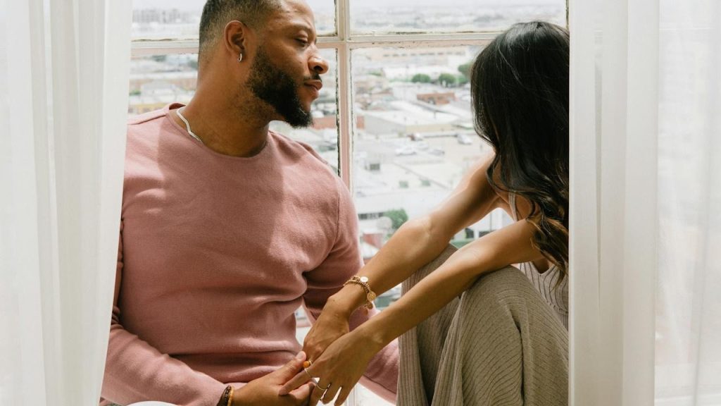 A man and a woman sitting on a windowsill.