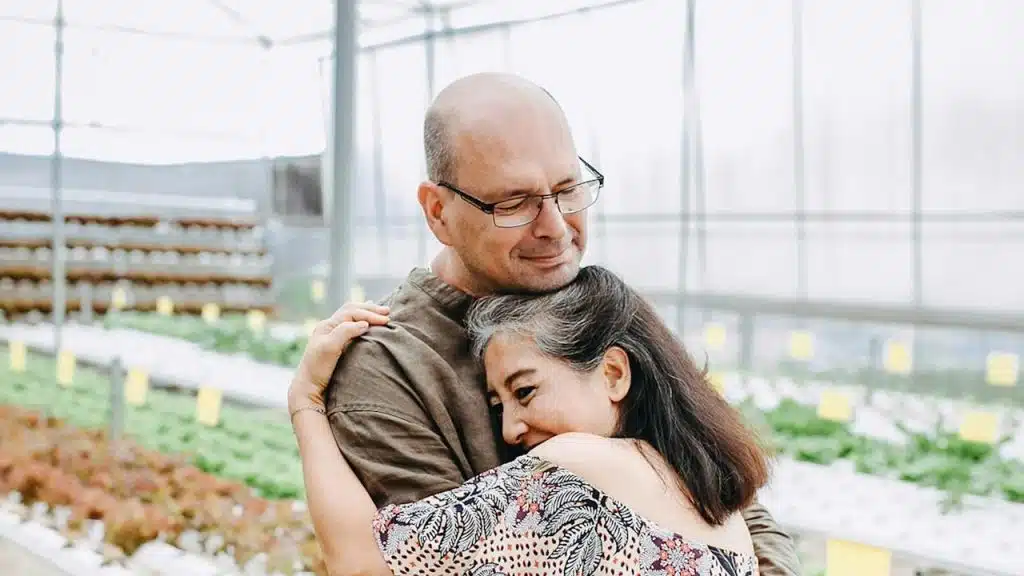  mature couple hugging in a greenhouse.