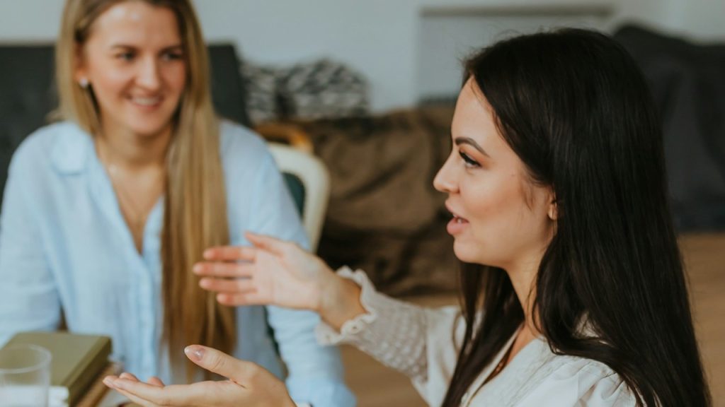 A woman talking to another woman while sitting at a table.