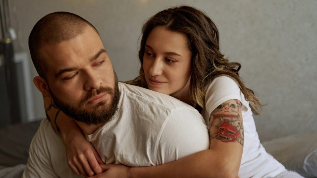 A woman is hugging an angry man from behind.