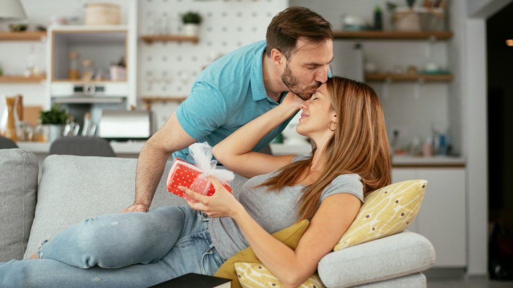 A man giving a present to his wife while kissing her on her forehead.
