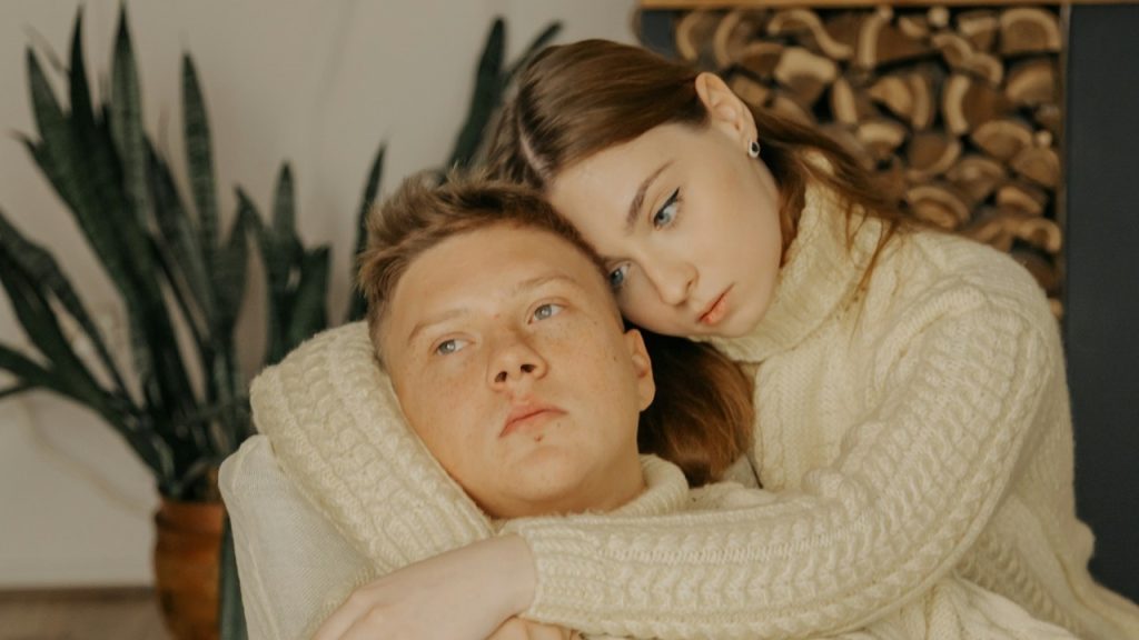 A woman hugging her man while sitting indoors.