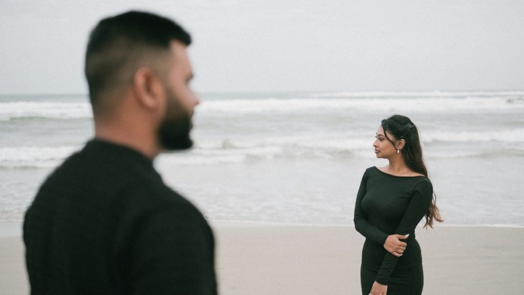A couple standing apart from each other on a beach.