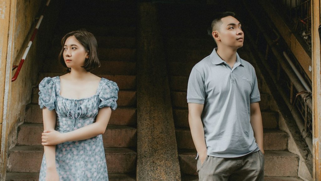 A couple standing apart from each other at the base of some stairs and looking in opposite directions.