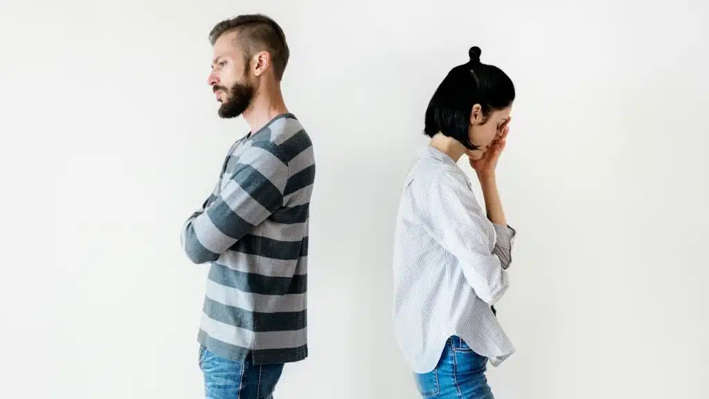 A couple standing with their backs to each other and refusing to talk while the woman looks especially upset.