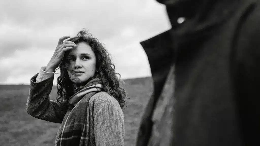 A black-and-white photo of a woman standing next to a man wearing a black coat.