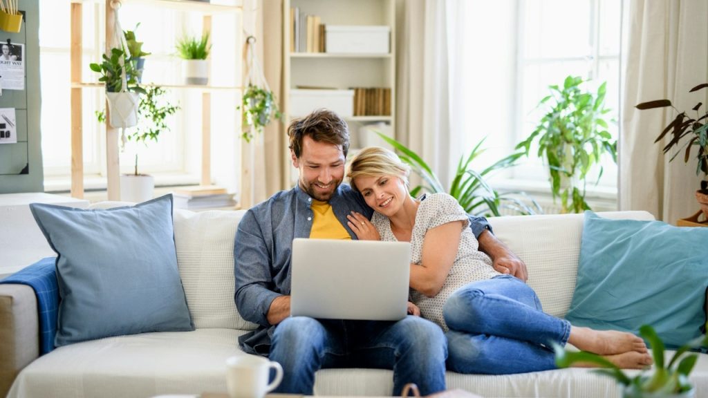 A couple on a couch looking at a laptop.