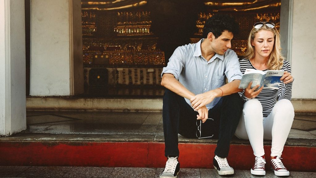 A couple sitting on stairs and reading a book.