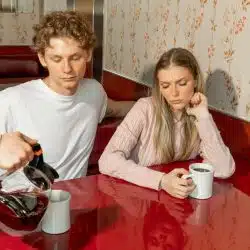 A waiter pours coffee in a mug while a couple is watching silently.