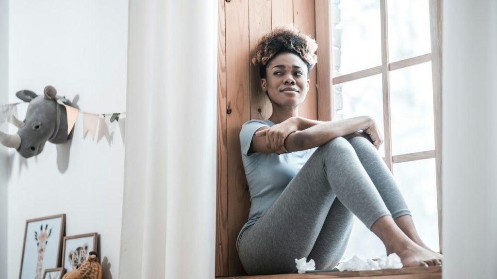 A crying woman sitting on a window sill.
