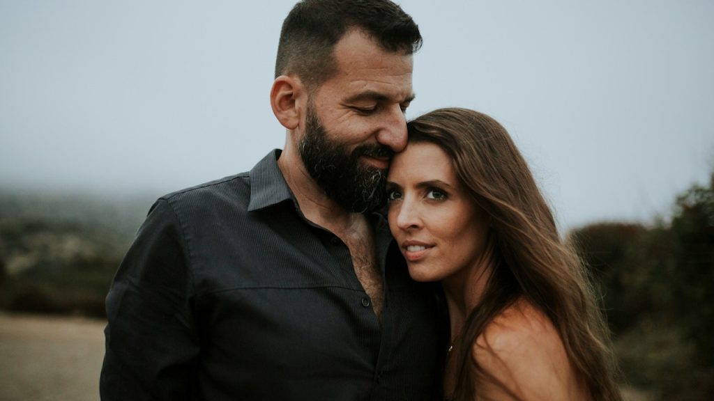 A bearded man and woman standing close to each other outdoors.
