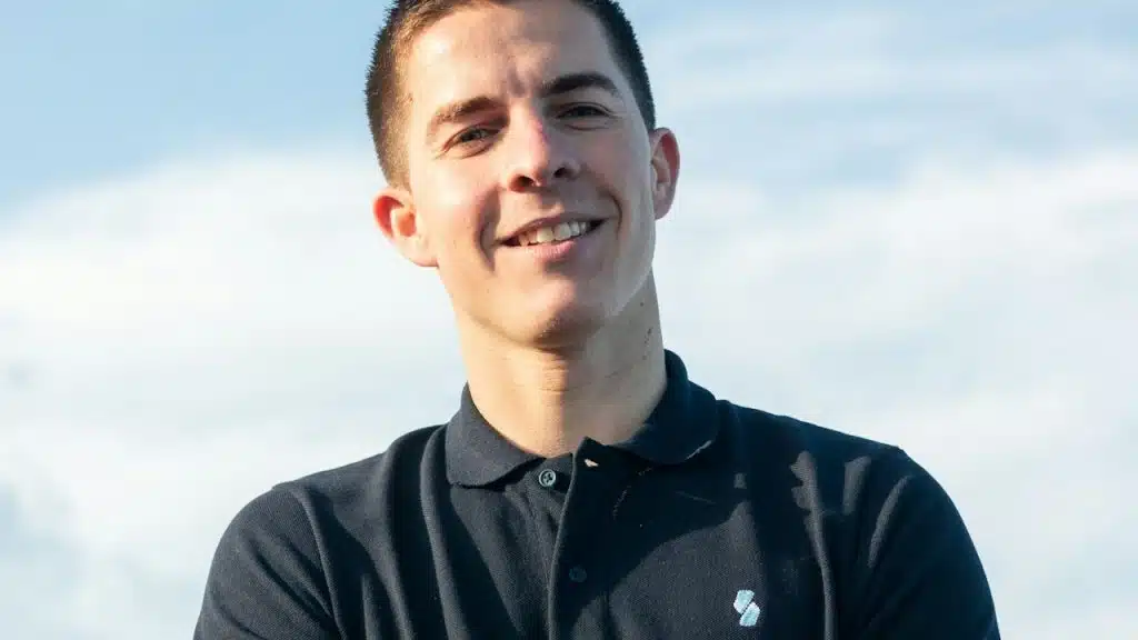 A man wearing a black polo shirt is standing under the sky.